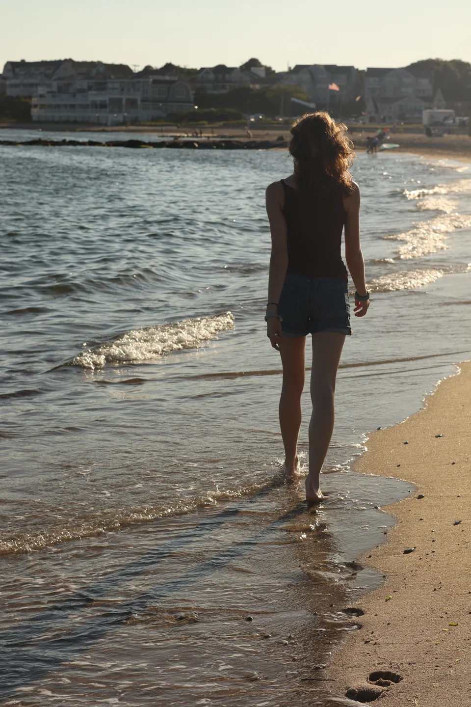 A woman walking along the shoreline in warm evening light.