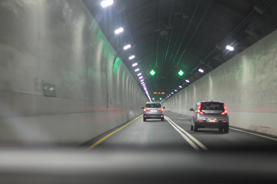 Cars traveling through a tunnel beneath rows of white lights and green arrows.